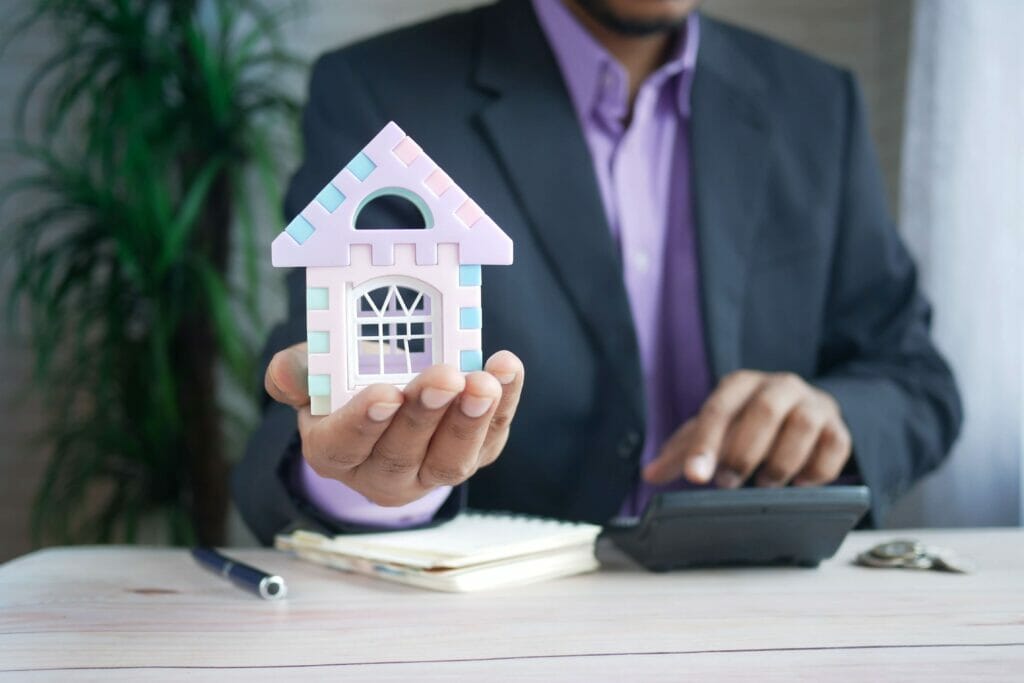 Close-up of a man holding a small model of a front door to a house to symbolize a home.
